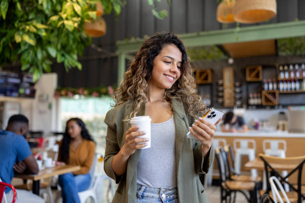Woman leaving a cafe with a coffee to go while using her cell phone