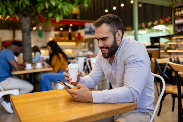 istock Happy man using his cell phone while drinking a cup of coffee at a cafe 2193767399
