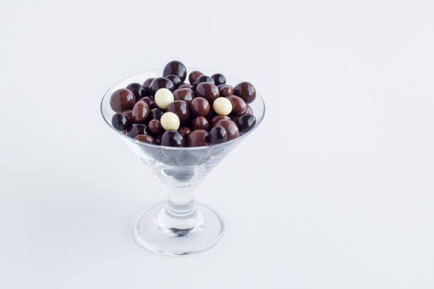 Elegant dark ball chocolates in glass candy bowl at white with copy space.