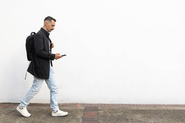 istock Businessman with backpack is on his phone while walking against white wall 2193769514