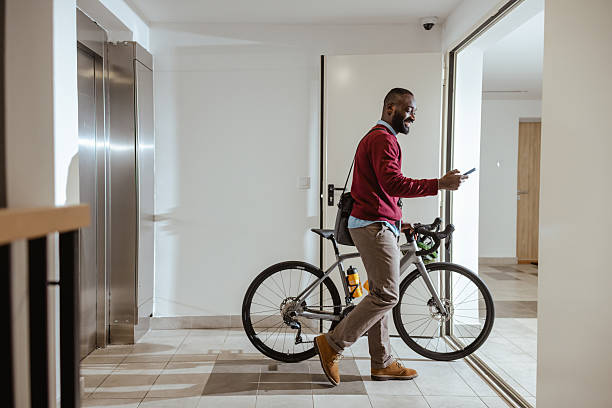 Man walking indoors with a bicycle in modern apartment building and using smartphone