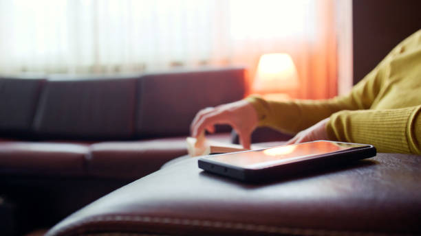 Smart home appliances and energy efficient house upgrades. Woman reading a book, turns on smart lights at home controlled from mobile app through smartphone.