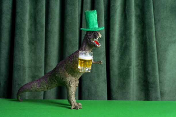 Funny dinosaur in green hat with beer celebrating St. Patrick's day. stock photo
