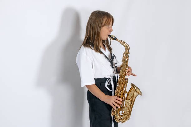 istock Girl playing, practicing the saxophone, playing a melody on a musical instrument, standing against the white background. Out-of-school children activities, lessons 2193812228