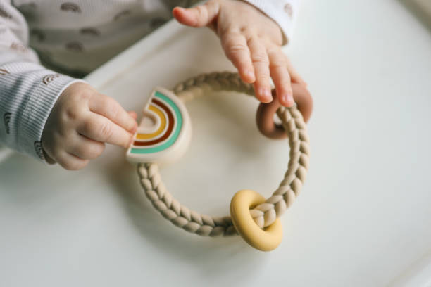 istock Baby holding a silicone rainbow teether with braided handle and pastel-colored details. Perfect for sensory play and teething relief. Modern and functional design 2193813847
