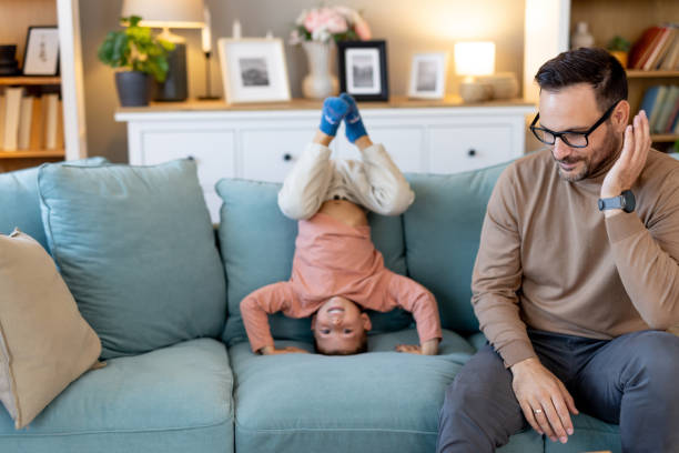 istock Child on couch upside down while dad smiles, enjoying fun time 2193818053