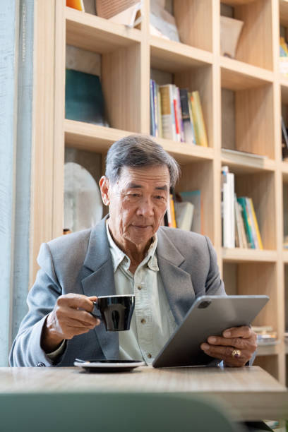 istock Thoughtful senior man holding coffee and using a tablet in a cozy library like cafe 2193819315