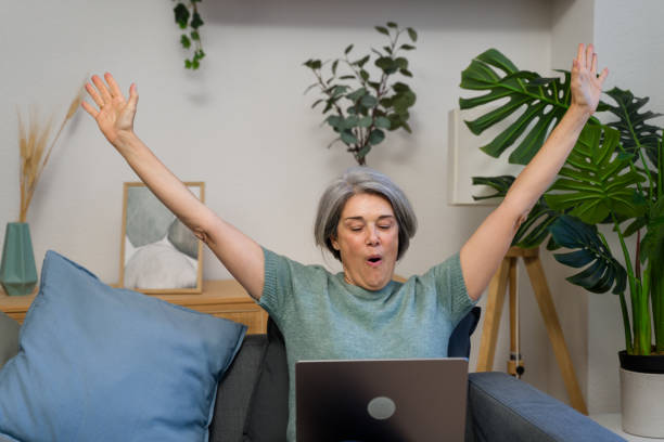 istock Excited mature woman celebrating success while using laptop at home 2193825299
