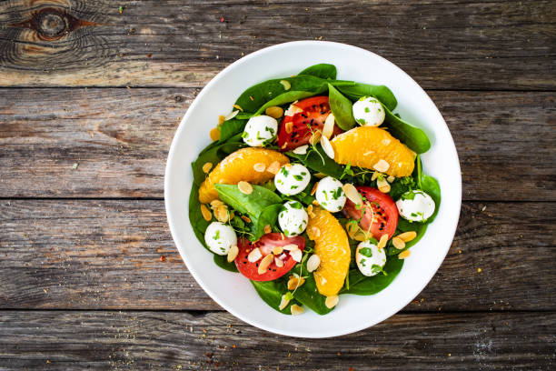 istock Mozzarella salad with leafy greens, orange and tomatoes on wooden table 2193828992