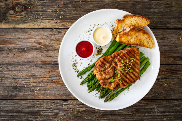 Pork loin steaks and cooked green asparagus on wooden table