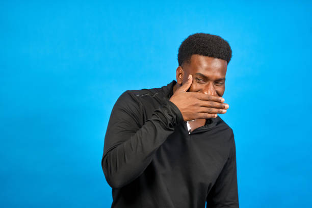 istock Young man covering his mouth while laughing on blue background 2193839851