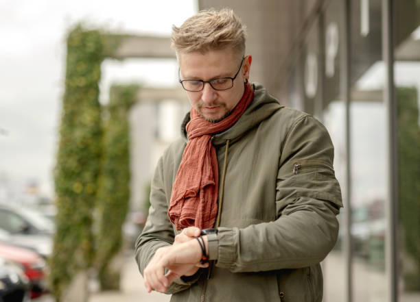 Modern businessman with beard looking at watch and walking on the city street.