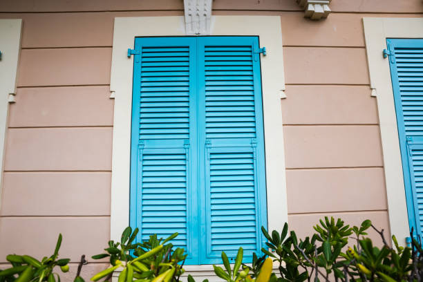 Window with closed wooden shutters painted blue installed in light brown wall, view outdoors in overcast day