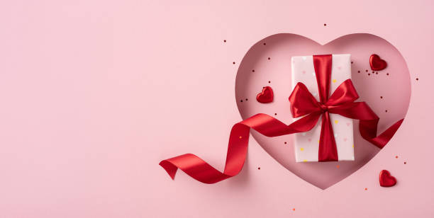istock A beautifully wrapped Valentine's Day gift with a red ribbon, placed within a heart-shaped cutout, symbolizing love and romance. The pink background adds to the festive and romantic atmosphere 2193847904