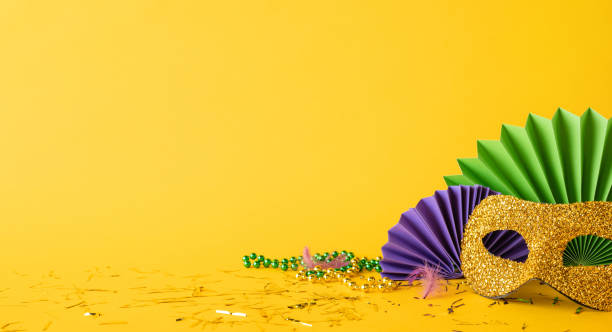 istock Festive side view setup featuring a golden glitter mask with decorative colored fans and beads against a yellow background, symbolizing the vibrant and joyful spirit of Mardi Gras celebrations 2193847920