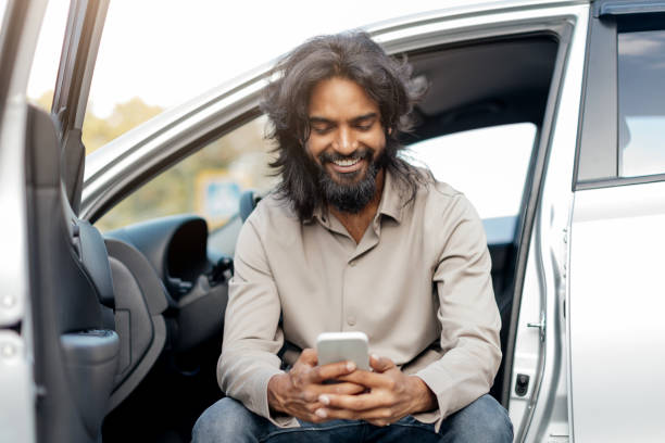 istock Happy smiling middle eastern man typing a message on the phone while sitting in the car. 2193850024