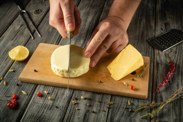 istock Hands skillfully slice through a creamy cheese wedge on a wooden board adorned with fresh herbs, spices, and a lemon. The rustic setting exudes a warm, inviting atmosphere 2193852522