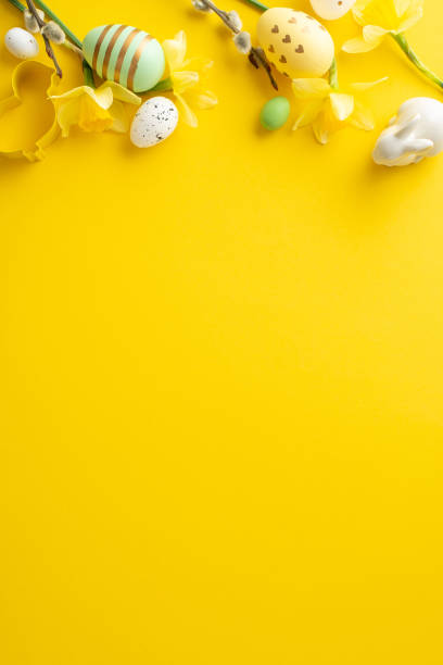 istock Easter vertical concept featuring colorful eggs, bunny figurines, and spring flowers on a yellow background 2193856398