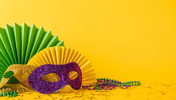 Mardi Gras side view themed still life with a festive yellow background, featuring sparkling masks, decorative paper fans, and colorful beads, evoking celebration, joy, and cultural festivity