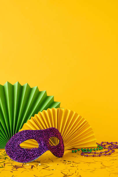 istock Colorful Mardi Gras side vertical view decorations displayed with a glittered mask, fans, and party beads on a vibrant yellow background featuring confetti and celebration elements 2193856443