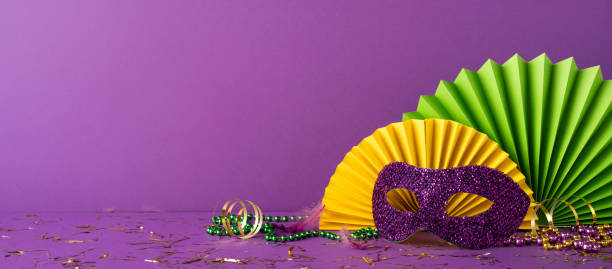 istock Festive Mardi Gras decorations arranged with a purple backdrop including beads, mask, and vibrant colored fans 2193856451