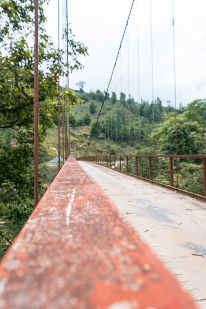 Sa Pa, Vietnam. A rusted metal frame suspension bridge with a concrete path, set in a green, hilly landscape surrounded by trees and vegetation.