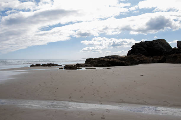 istock Empty sandy beach with footprints, scattered rocks, calm ocean waves, and a partly cloudy sky creating a peaceful atmosphere. 2193880775