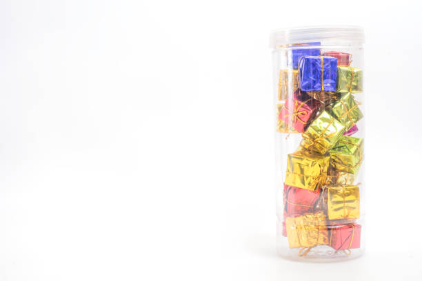 A pile of small, colorful gift boxes wrapped in shiny paper and arranged in a clear container, set against a vibrant white background. Perfect for holiday themes, festive celebrations.