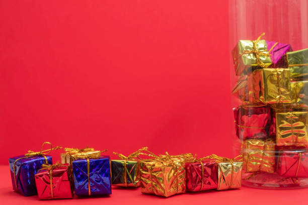 Brightly wrapped miniature gift boxes with golden ribbons are displayed against a red background, perfect for promoting holiday events, festivities, and gift-giving occasions.