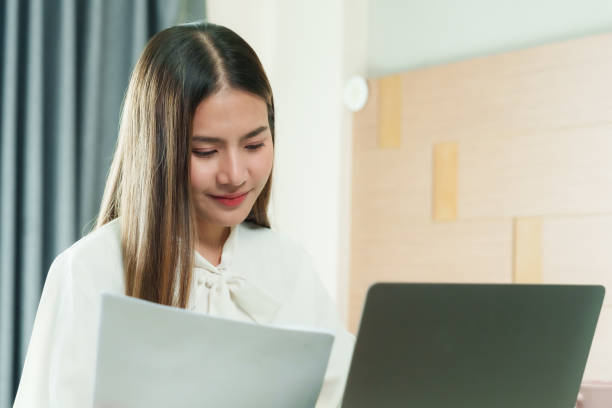istock Asian female office worker reviewing documents at home, maintaining focus and determination while working remotely in a comfortable and relaxed atmosphere. 2193887600