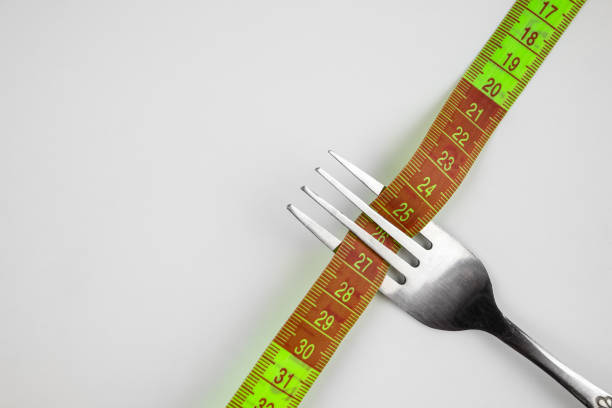 istock Measuring tape threaded by a fork on a white background. Good proper nutrition. Medical fasting. The concept of a diet for weight loss. Healthy lifestyle. Copy space. 2193889446
