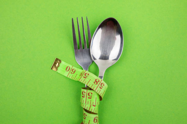 Steel spoon, fork and measuring tape on a green background.