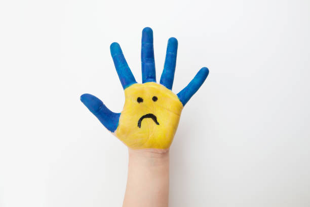 istock Blue and yellow painted children's hand with a sad emoticon isolated on white. Support for Ukraine. Stop the war in Ukraine. 2193890457