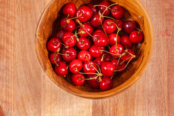small glass bowl filled with cherries, covered with drops of water on wooden board, backlit