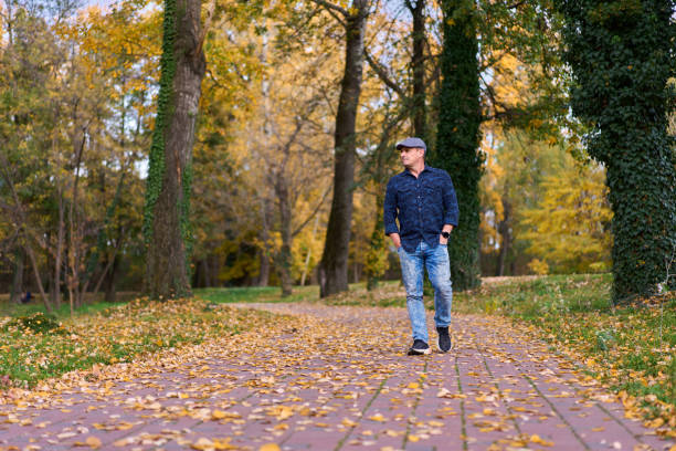 Middle aged man taking a walk in the park with colorful autumn leaves everywhere