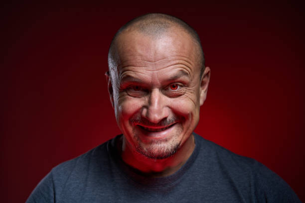 Menacing and sinister man with red eyes and haunting evil smile, closeup over red background