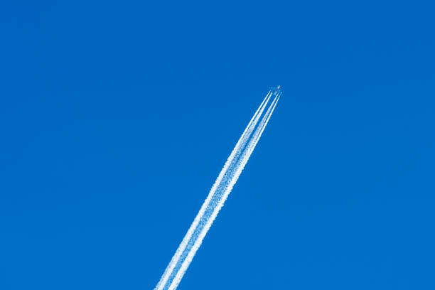 An airplane climbs high into the clear blue sky, leaving behind visible vapor trails. The bright atmosphere showcases the vehicle in motion and highlights the beauty of flight.