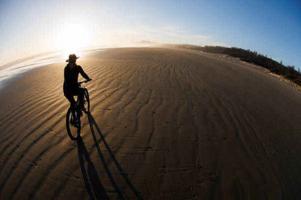 A woman goes for a bicycle ride at low tide on Long Beach on Vancouver Island near Tofino, British Columbia, Canada, at sunset.
