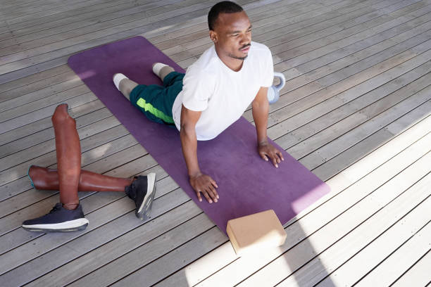Man with amputated legs stretching on yoga mat on patio