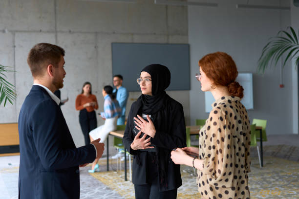 istock A diverse group of business professionals engages in a conversation during a work break in the office, with their colleagues visible in the background, fostering collaboration and connection 2193897494