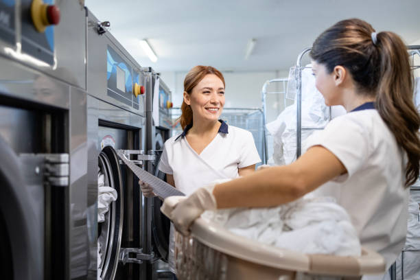 istock Female cleaning workers loading washing machine with dirty laundry. 2193900844