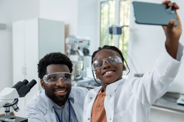 istock Happy teacher and student in lab coats making selfie on a phone 2193901972
