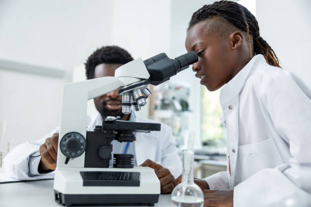 istock Dark-skinned schoolgirl in a lab coat looking into microscope and looking involved 2193902020