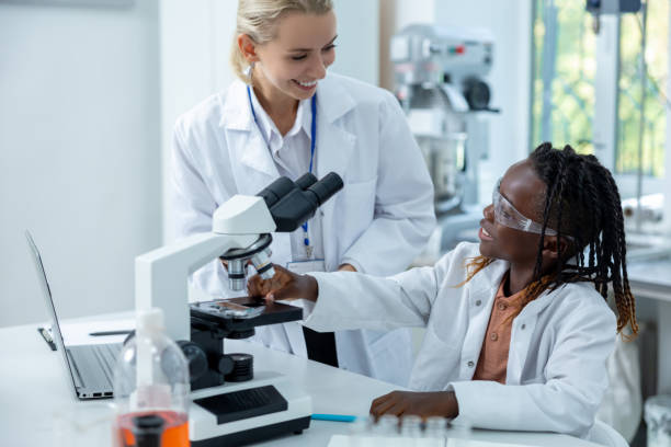 istock Blonde teacher in white lab explaining how to work with microscope to a student 2193902083