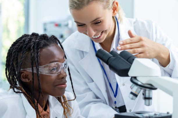istock Blonde teacher in white lab explaining how to work with microscope to a student 2193902084