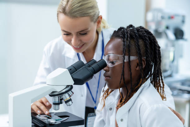 istock Blonde teacher in white lab explaining how to work with microscope to a student 2193902086