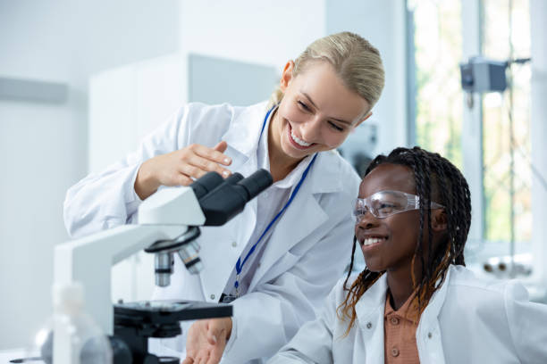 istock Blonde teacher in white lab explaining how to work with microscope to a student 2193902089