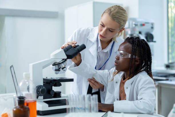 istock Blonde teacher in white lab explaining how to work with microscope to a student 2193902090
