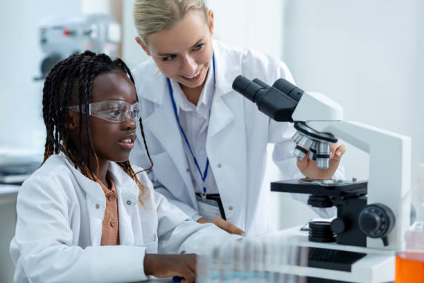 istock Blonde teacher in white lab explaining how to work with microscope to a student 2193902093