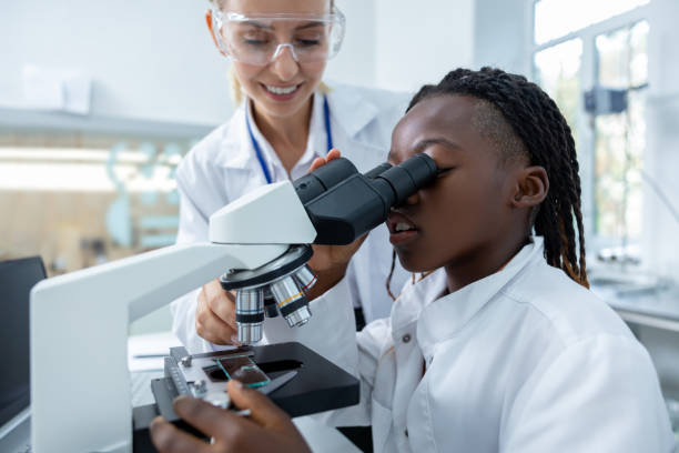 istock Blonde teacher helping a student in a protective glasses to scrutinize substance in a microscope 2193902148